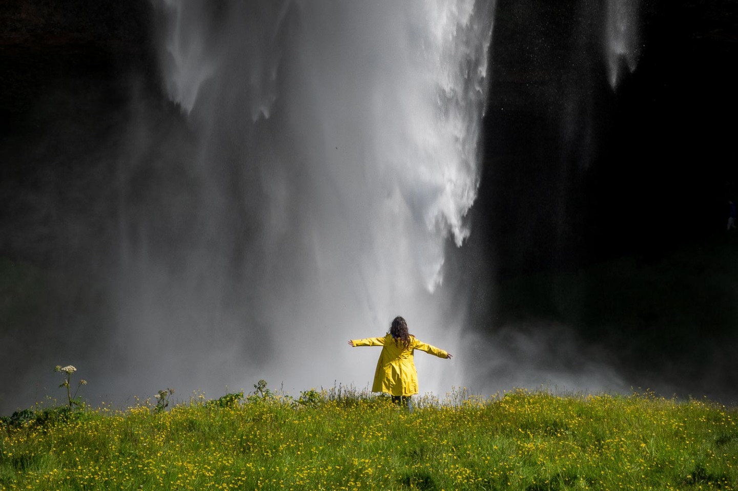 A girl standing under the waterfall, Seljalandfoss, Iceland.